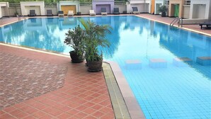 A swimming pool with tiled edges, potted plants, and lounge chairs.