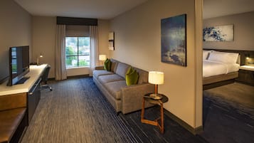 A hotel room with a desk, a sofa, a bed, a window with curtains, and artwork on the walls.