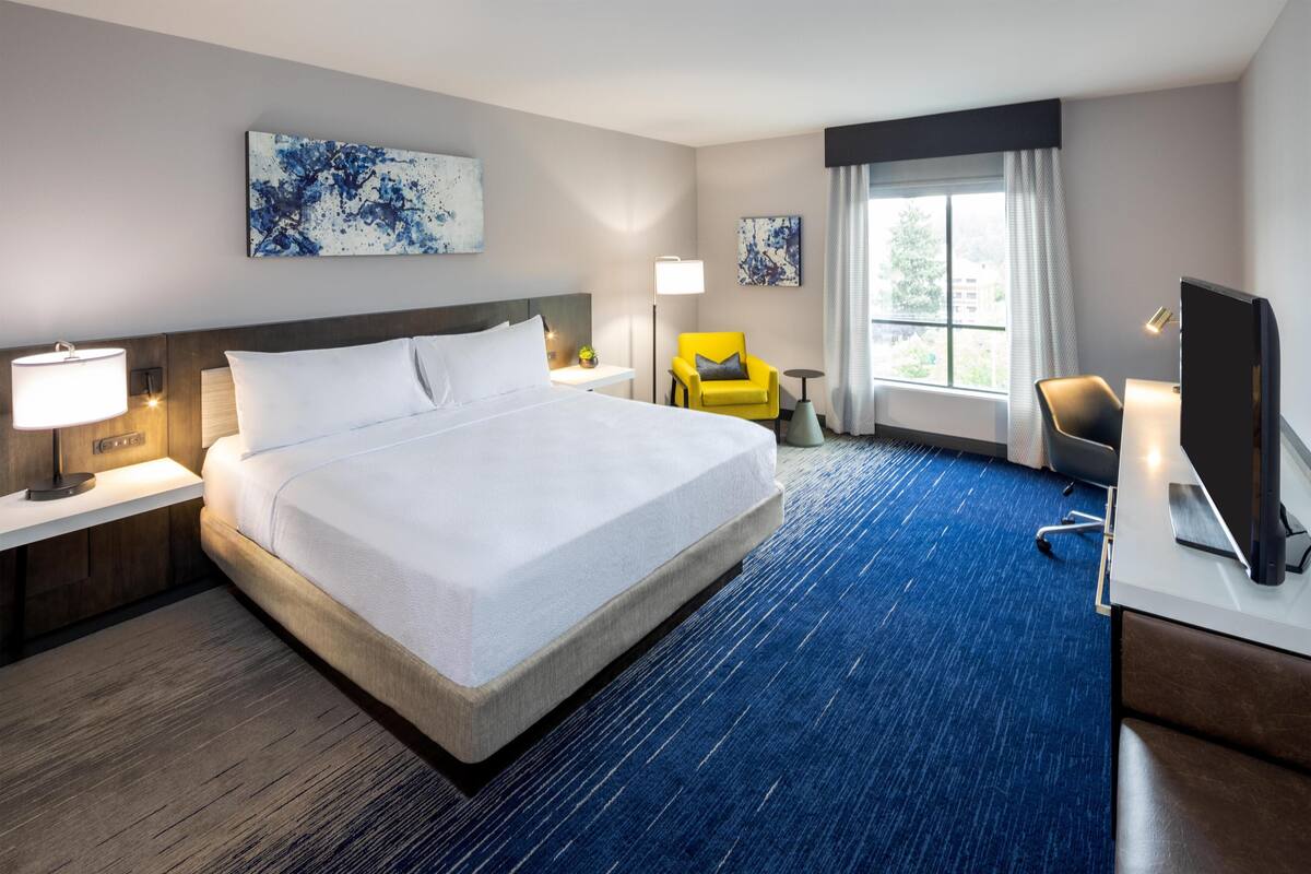 A hotel room with a large bed, a desk with a computer, a chair, and artwork on the walls.