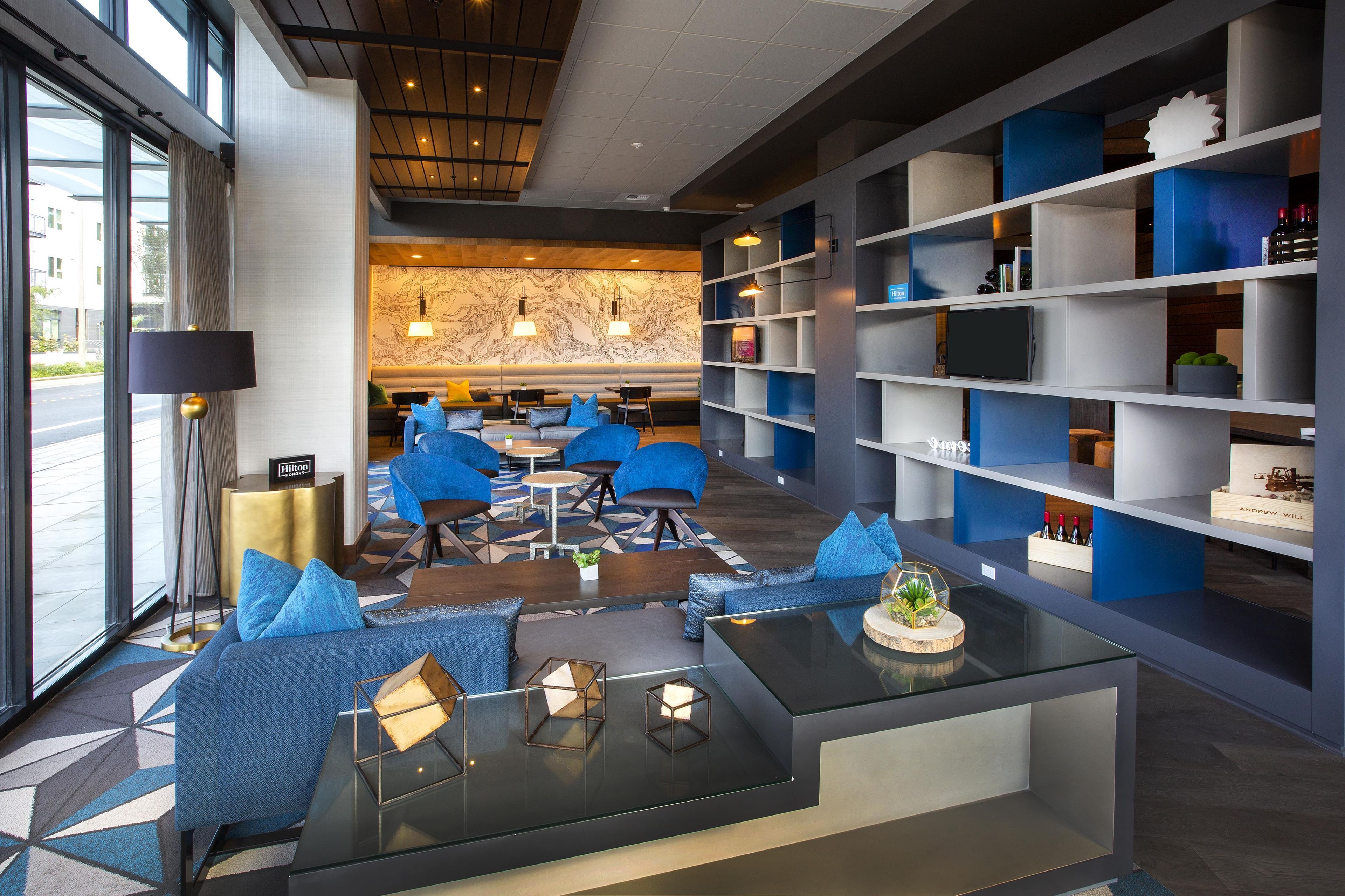 A modern hotel lobby with seating areas, a bar, and a bookshelf.