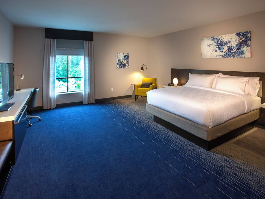 Une chambre d’hôtel avec un grand lit, un bureau avec une chaise, une petite table avec une lampe et des œuvres d’art accrochées aux murs.