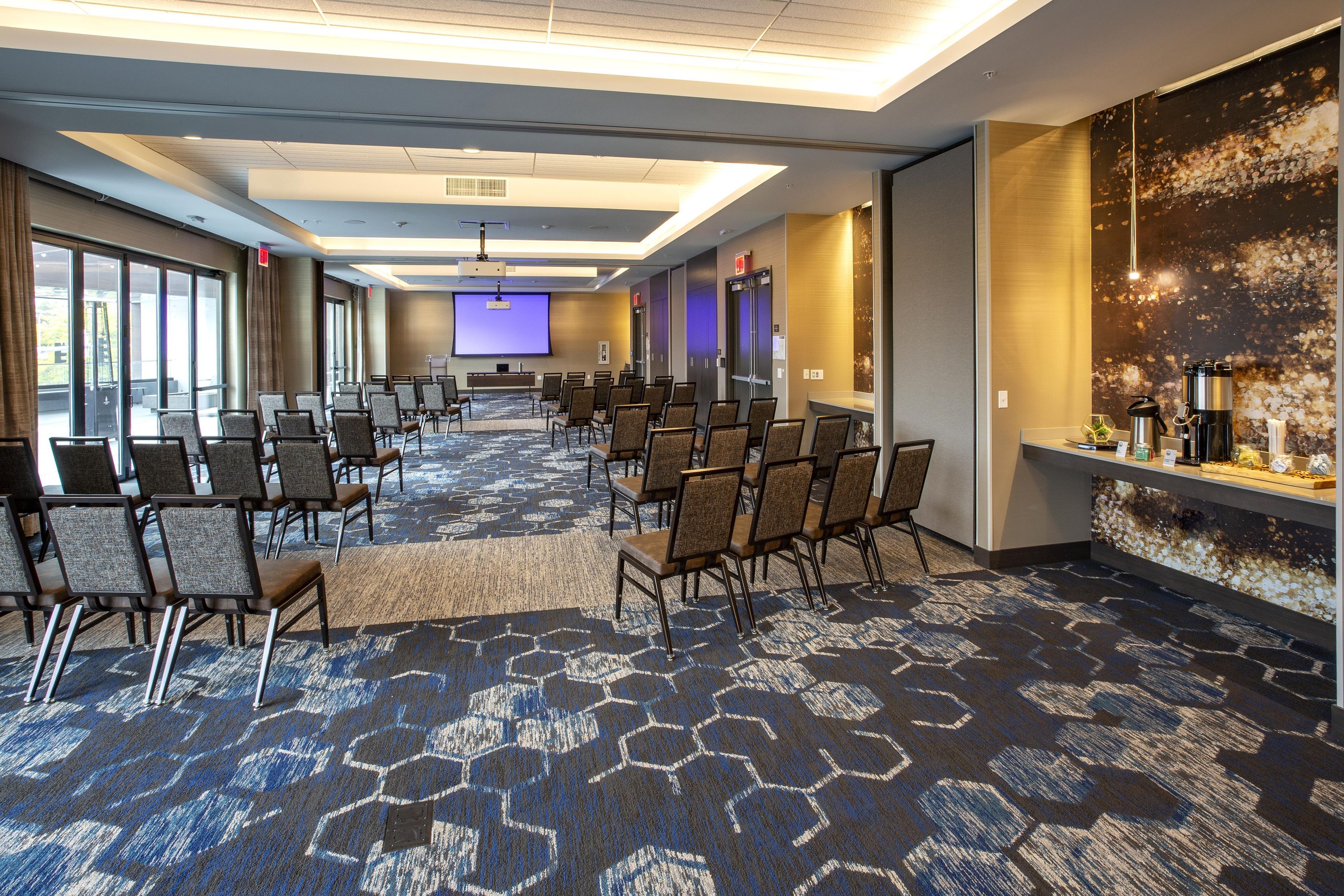 A conference room with rows of chairs, a large screen, and a reception desk.