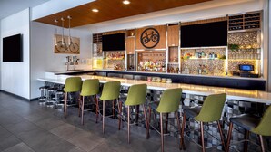 A modern bar area with a long counter, multiple stools, a television screen, and a bicycle-themed decor. - Hilton Garden Inn Redmond Seattle (Redmond)