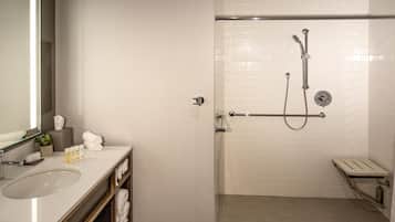 A modern bathroom with a sink, mirror, towel rack, and a walk-in shower with a grab bar.