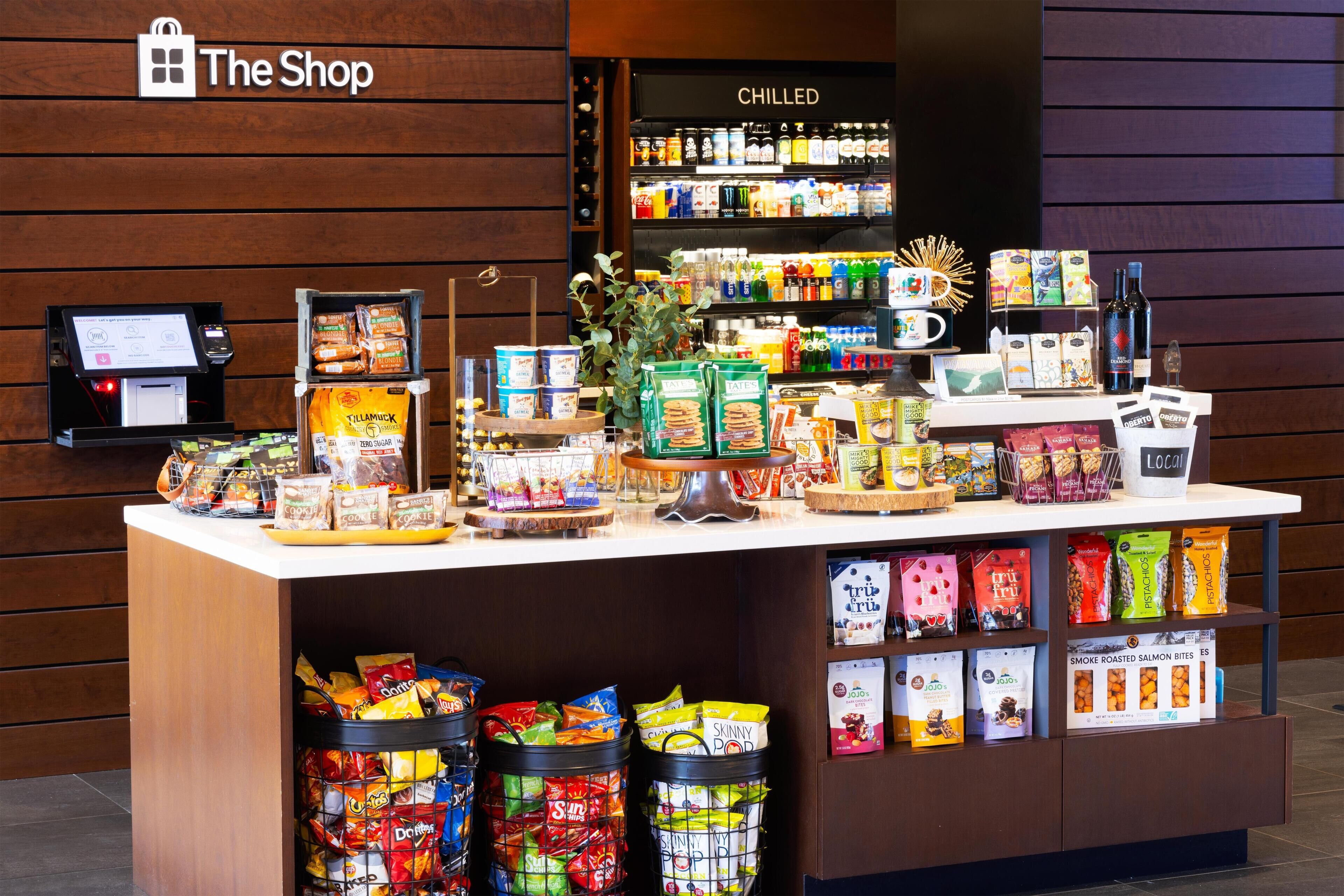 A snack display in a store with various packaged snacks and a refrigerated section in the background.