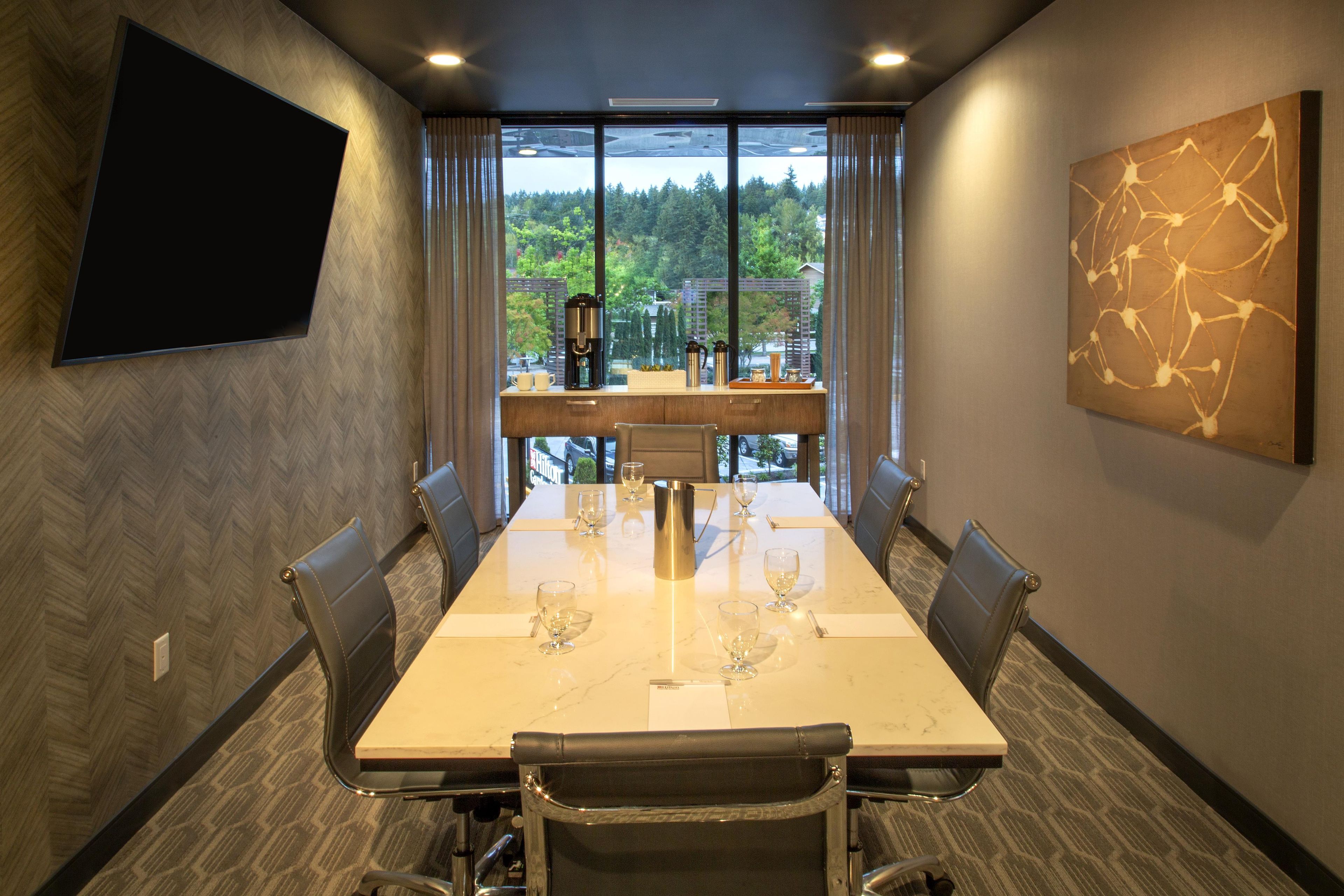 A conference room with a large table, chairs, a coffee machine, and a painting on the wall.