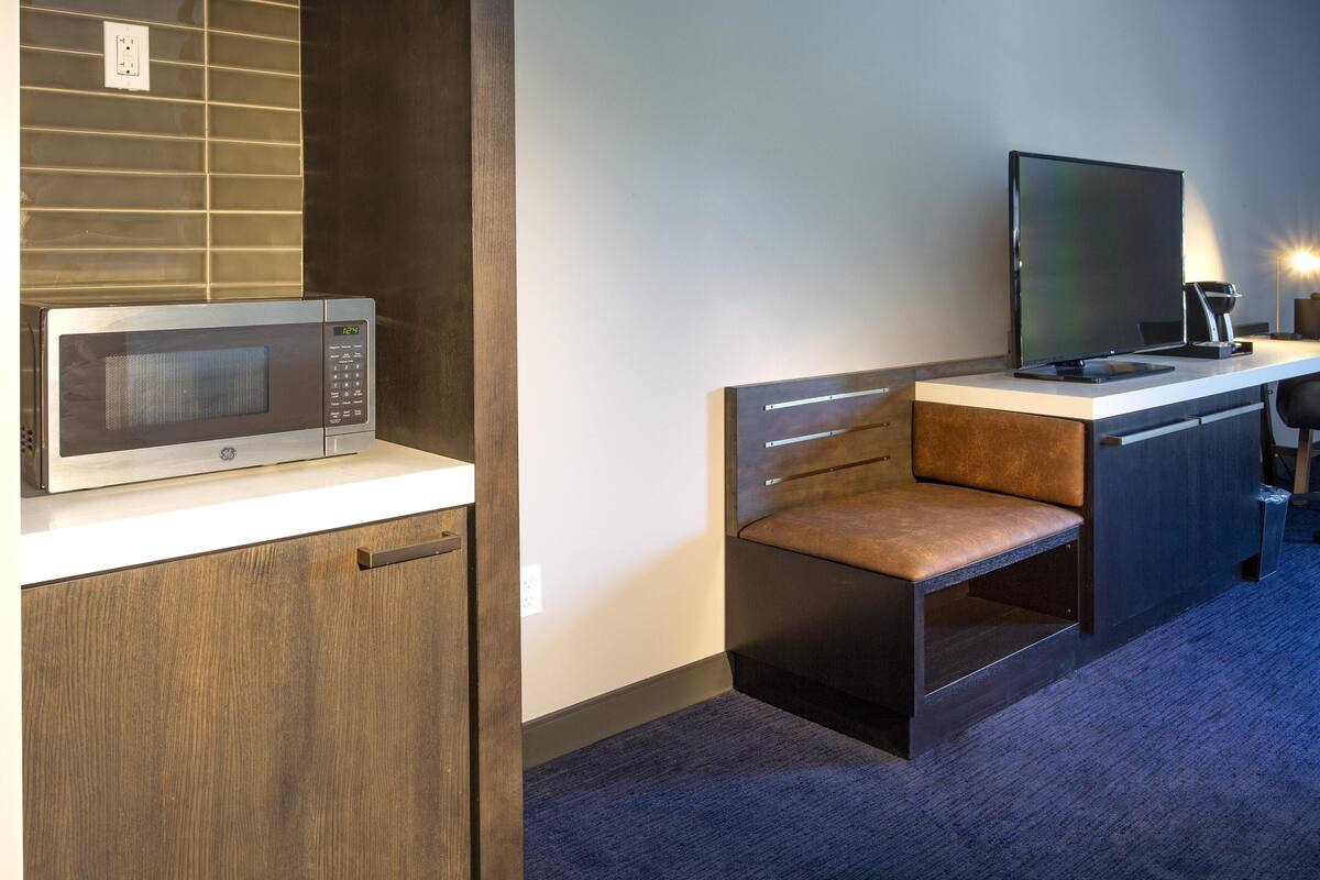 A compact kitchenette with a microwave, a flat-screen TV, and a small seating area.
