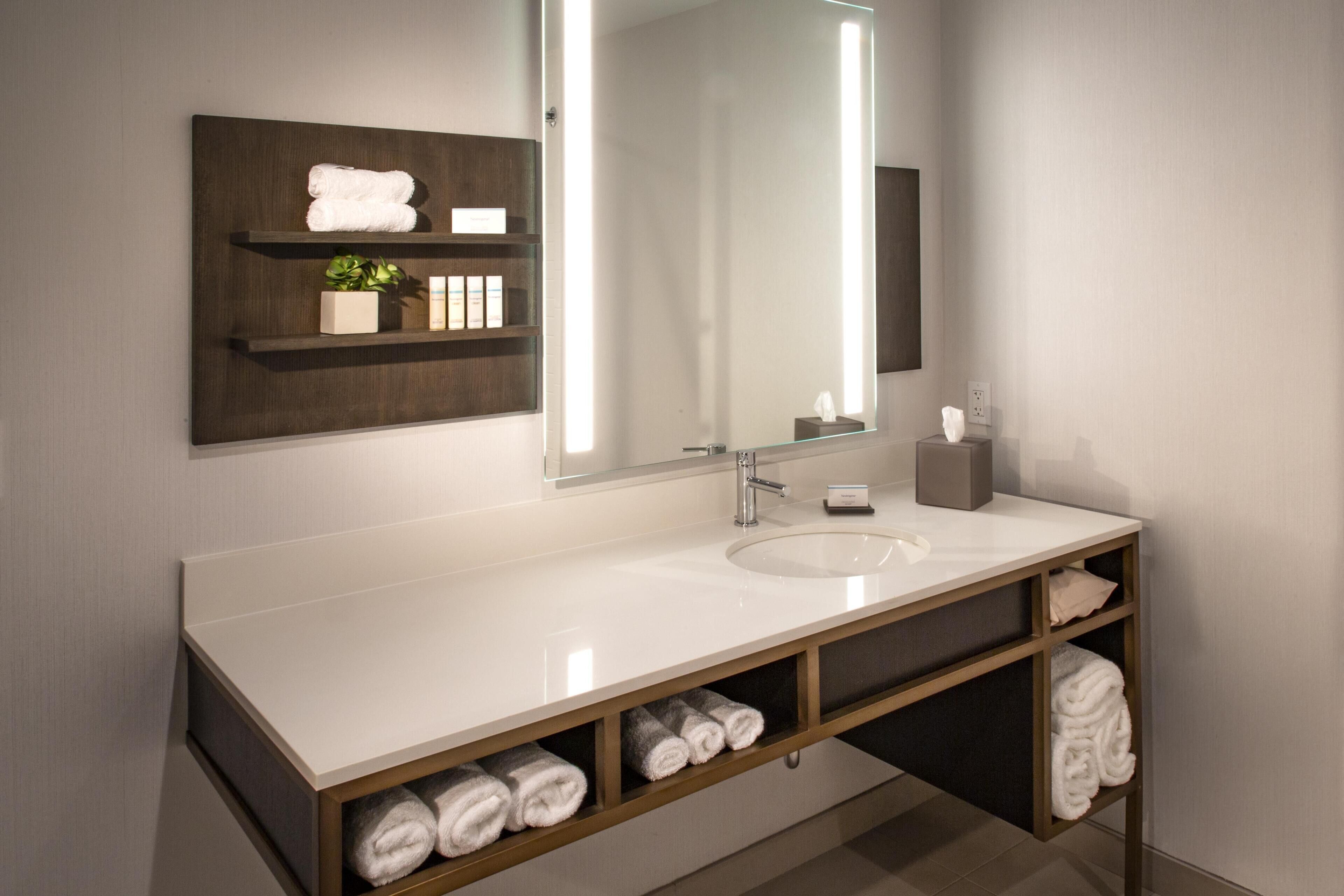 A modern bathroom with a white sink, a large mirror, and shelves with towels.