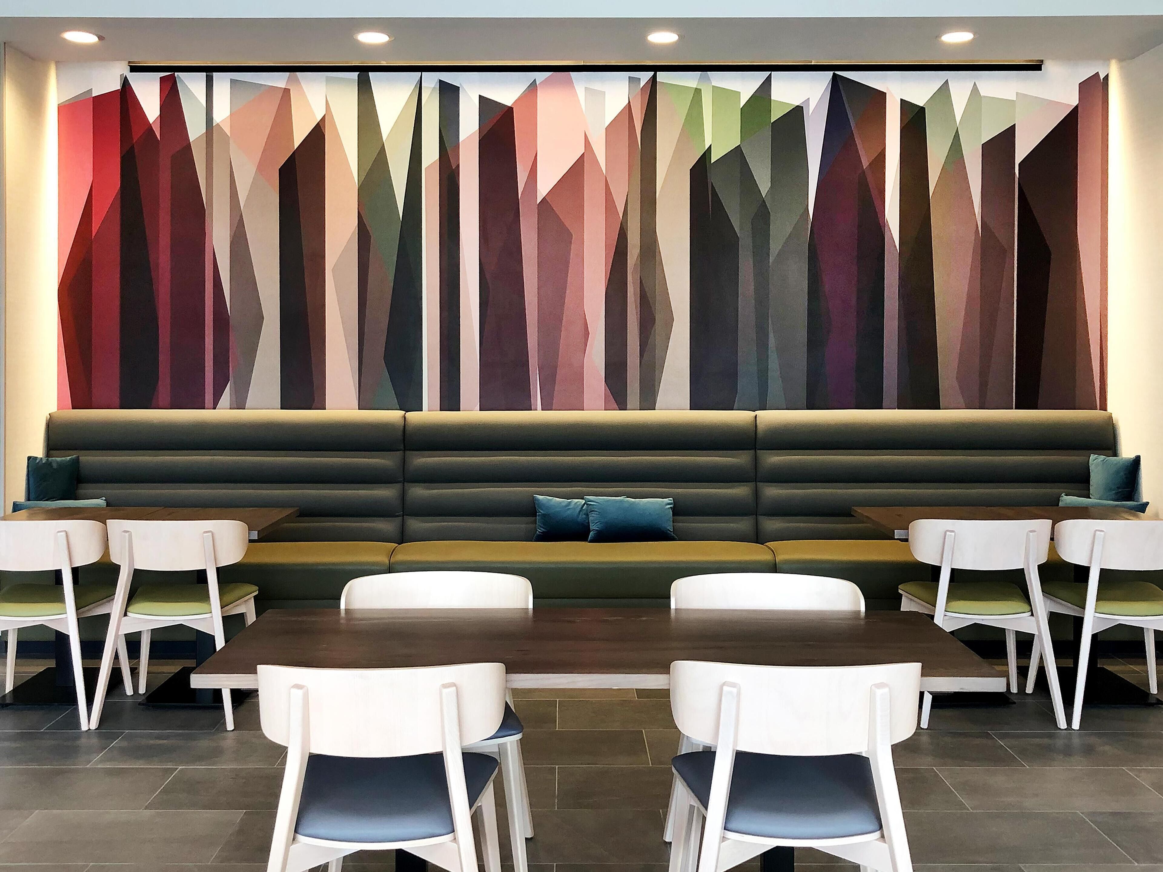 A modern dining area with a long table, white chairs, and a green cushioned bench.