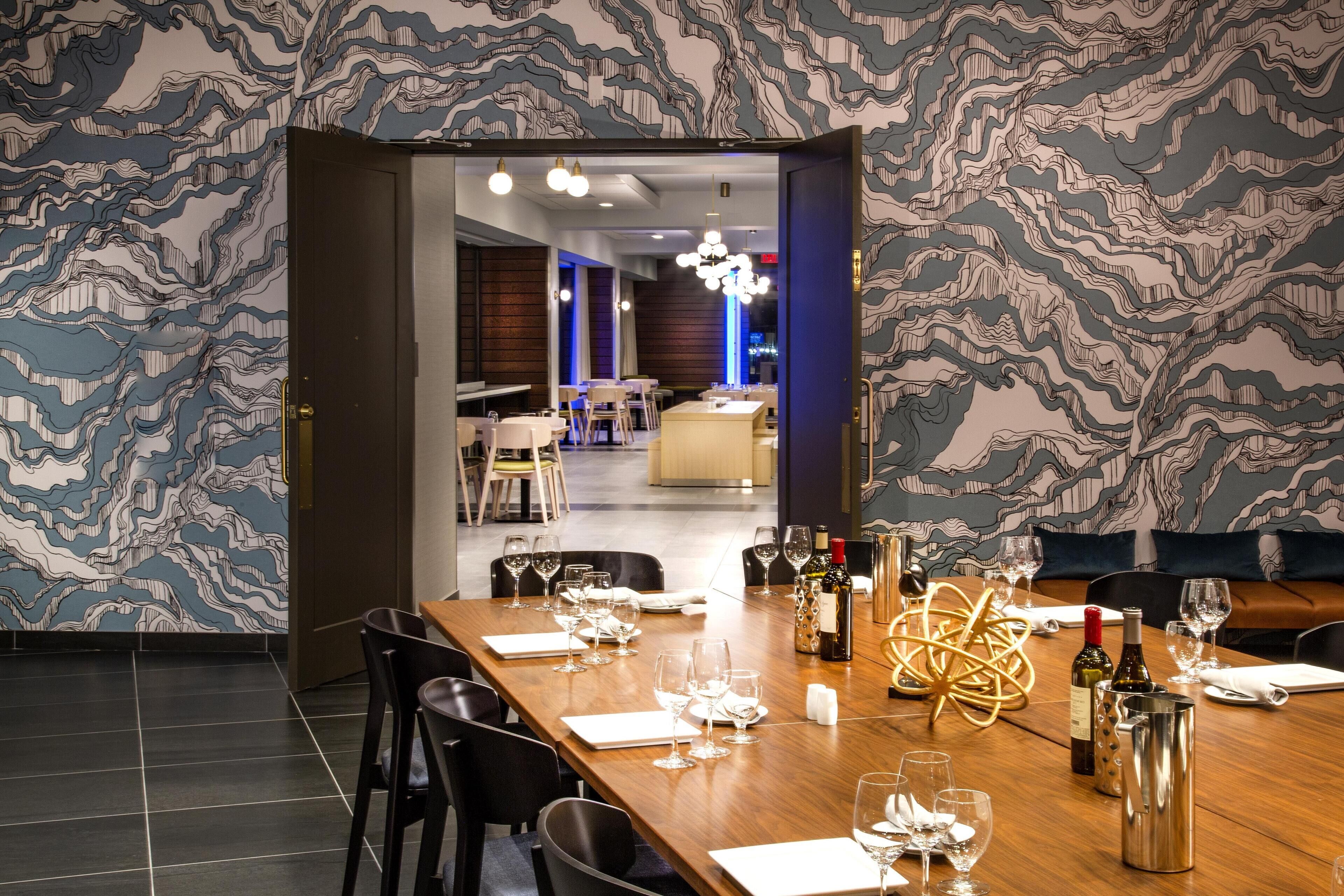 A dining area with a long table set for a meal, a chandelier, and a patterned wall.
