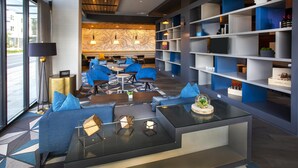 A modern hotel lobby with a seating area, a glass coffee table, and a bookshelf with various items. - Hilton Garden Inn Redmond Seattle (Redmond)