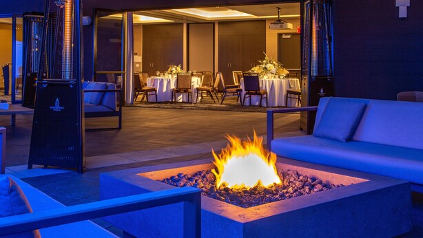 An outdoor seating area with a fire feature, tables set for dining, and a building entrance. - Hilton Garden Inn Redmond Seattle (Redmond)