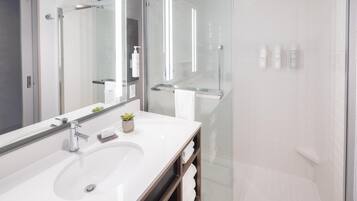 A modern bathroom with a glass shower enclosure, a large mirror, and a white sink.