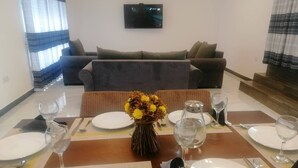 A dining area with a table set for four, a vase with yellow flowers, and a flat-screen TV on the wall. - Signature Kandy (Kandy)
