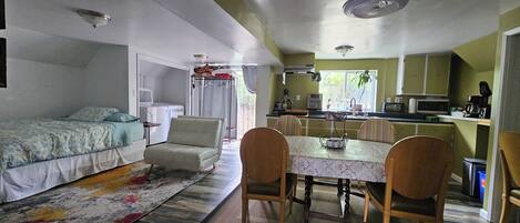 A compact living space with a bed, a sofa, a dining table with chairs, a kitchen area, and a ceiling fan.