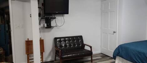 A room with a flat-screen TV mounted on the wall, a leather couch, a bed with a blue cover, and a patterned floor.