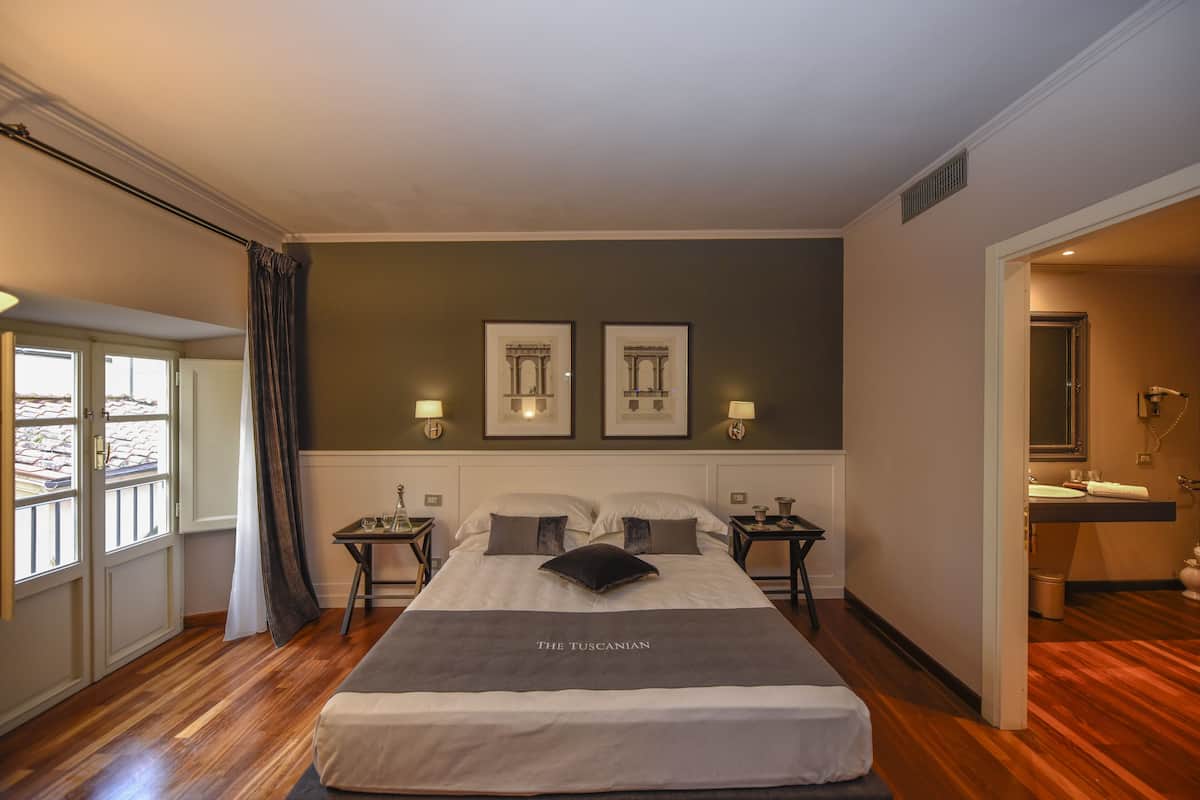 A hotel room with a large bed, two framed pictures on the wall, a nightstand with a lamp, and a bathroom visible through an open door.