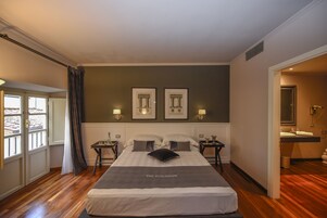 Una camera d'albergo con un letto grande, due quadri appesi al muro, un comodino con una lampada e un bagno visibile attraverso una porta aperta.