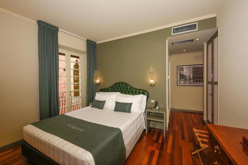 A hotel room with a bed, a nightstand, a wooden floor, and a door leading to another room.