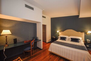 Una camera d'albergo con un letto, una scrivania, una sedia e un comodino.
