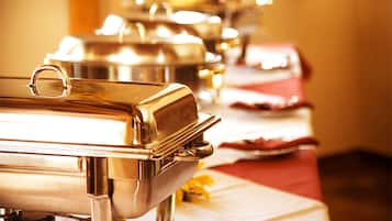 A buffet setup with stainless steel serving stations and a red tablecloth.