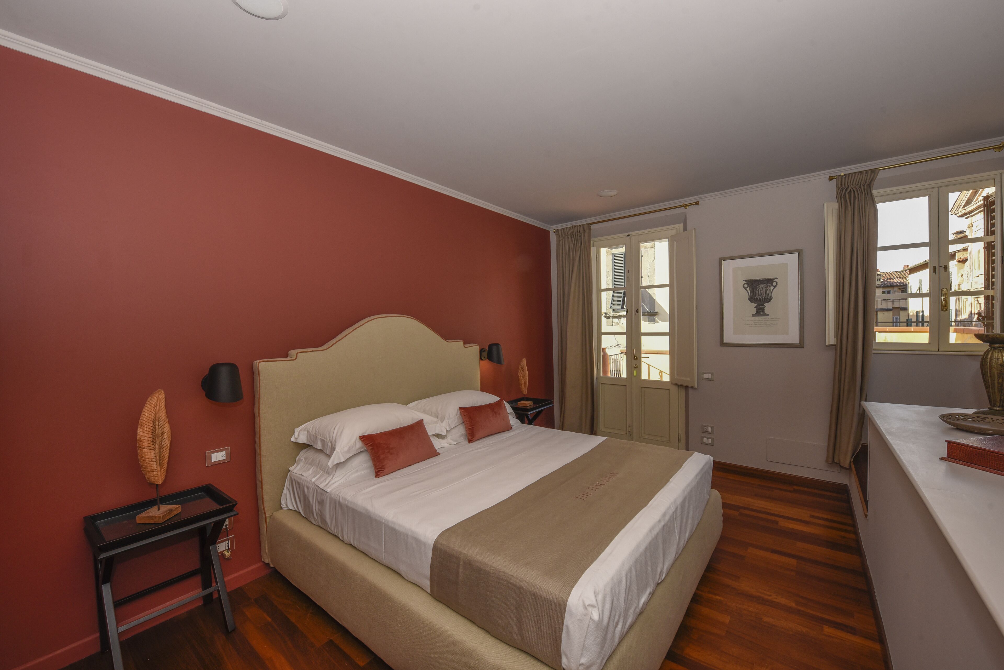 A bedroom with a bed, a nightstand, a lamp, a framed picture on the wall, and a window with curtains.