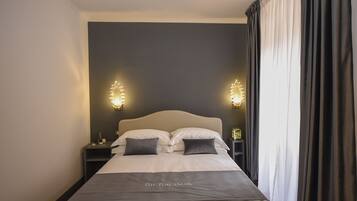 Una cama bien hecha con cabecera, dos mesitas de noche con lámparas y una cortina oscura en la ventana.