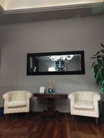 Quarto com duas poltronas estofadas, uma pequena mesa consola de madeira e um espelho na parede.