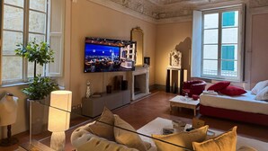 A living room with a television, sofa, red cushions, a glass coffee table, and a fireplace. - The Tuscanian Hotel (Lucca)