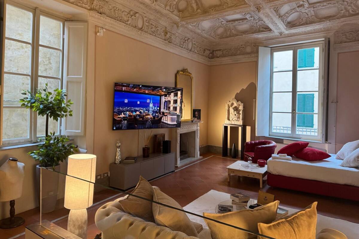 A living room with a television, sofa, red cushions, a glass coffee table, and a fireplace.