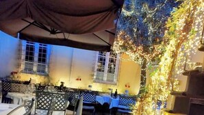 An outdoor patio area with tables and chairs, a wooden deck, and string lights. - The Tuscanian Hotel (Lucca)
