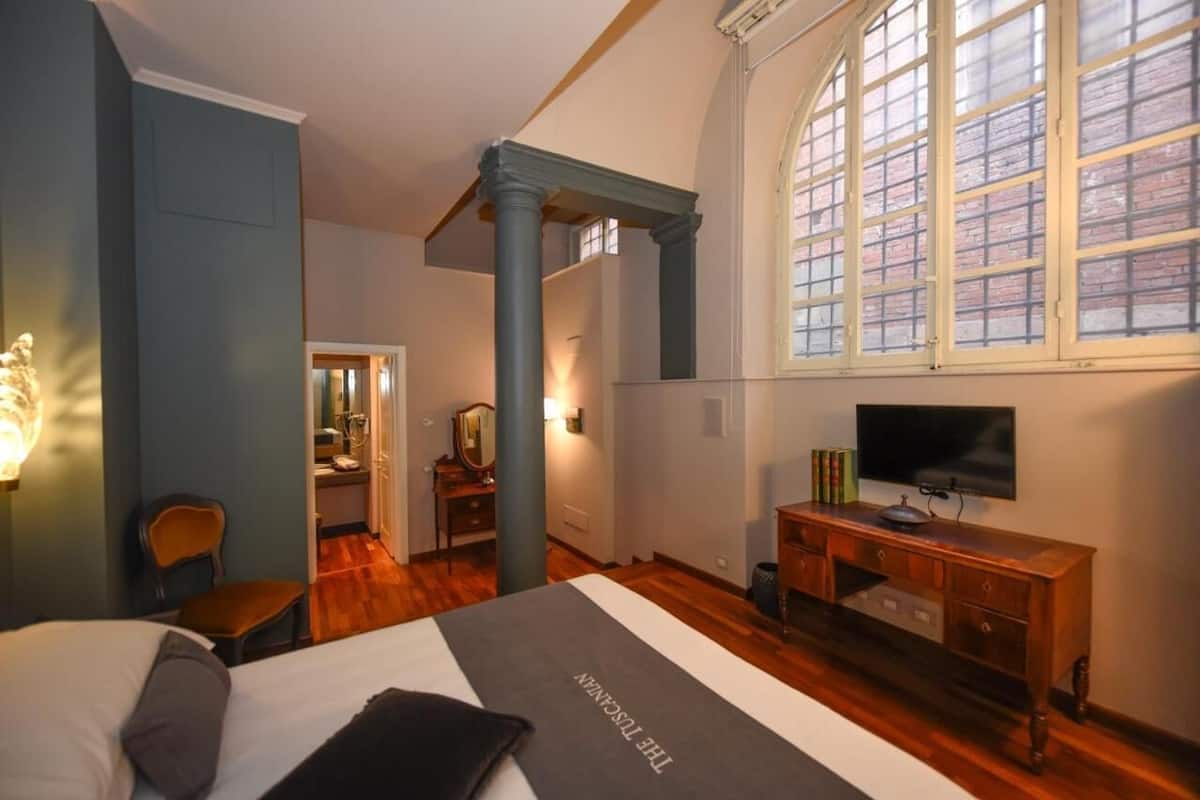 A hotel room with a bed, a desk, a television, and a large window with a view of the outside.