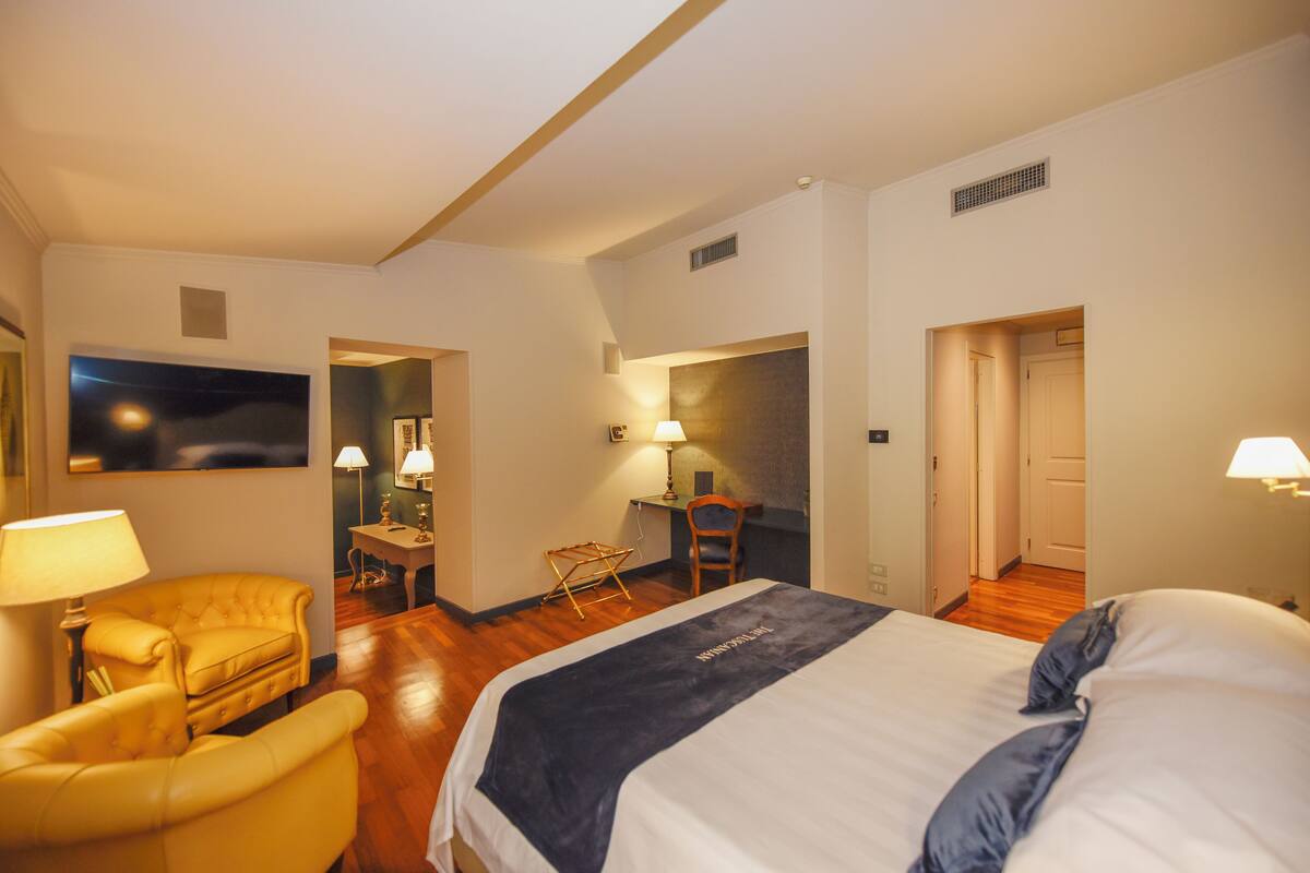 A hotel room with a bed, a chair, a desk, and a painting on the wall.