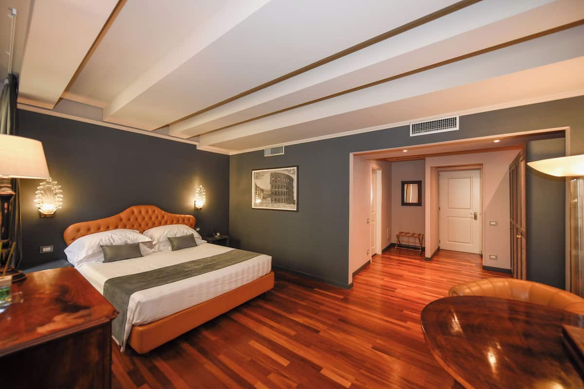 A bedroom with a large bed, wooden flooring, and a door leading to a bathroom.