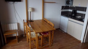 A compact kitchen with a wooden table and chairs, a microwave, a coffee maker, and a television mounted on the wall.