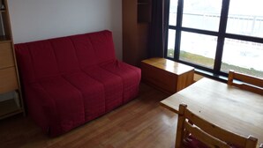 A room with a red sofa, a wooden table, and a window with a view of a bridge.