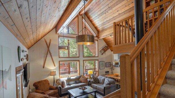 A spacious living room with a high ceiling, large windows, and a wooden staircase. - The Lodge: Comfort&Hospitality AC/4bdrm/10 beds/beach (Soda Springs)