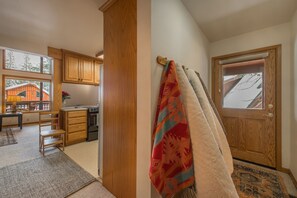 A kitchen with wooden cabinets, a dining area with a table and chairs, and a view of a cabin through large windows.