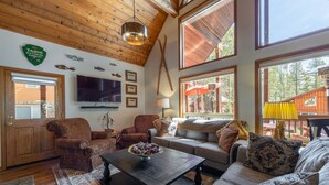 A cozy living room with wooden floors, a large TV, and a fireplace. There are two sofas and a coffee table. - The Lodge: Comfort&Hospitality AC/4bdrm/10 beds/beach (Soda Springs)