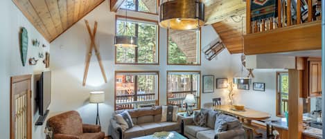 A spacious living area with high ceilings, wooden beams, and large windows offering views of the outdoors.