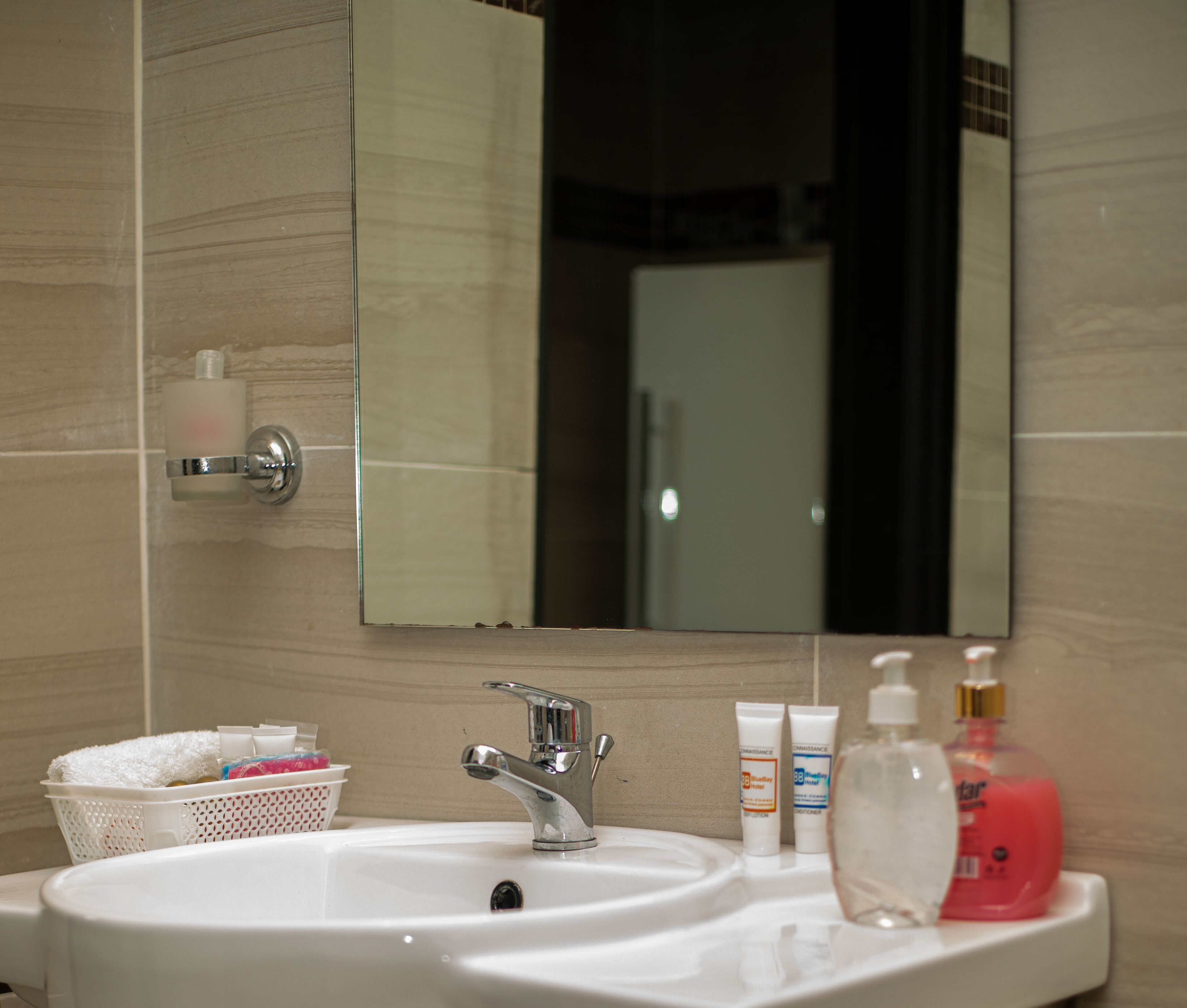 A bathroom sink with a mirror, toiletries, and a basket of towels.