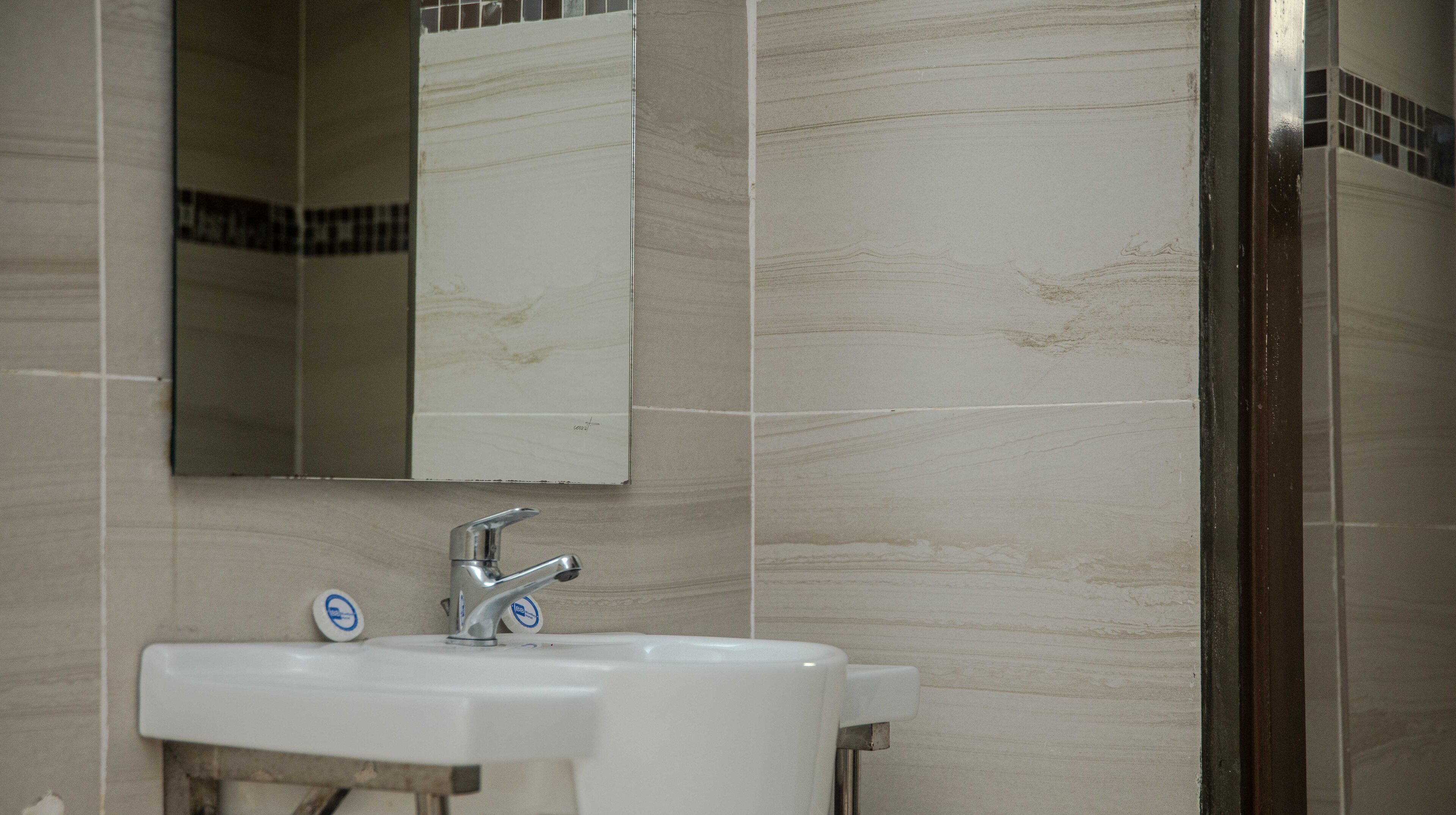 Un baño con un lavamanos blanco, un espejo y paredes con azulejos.