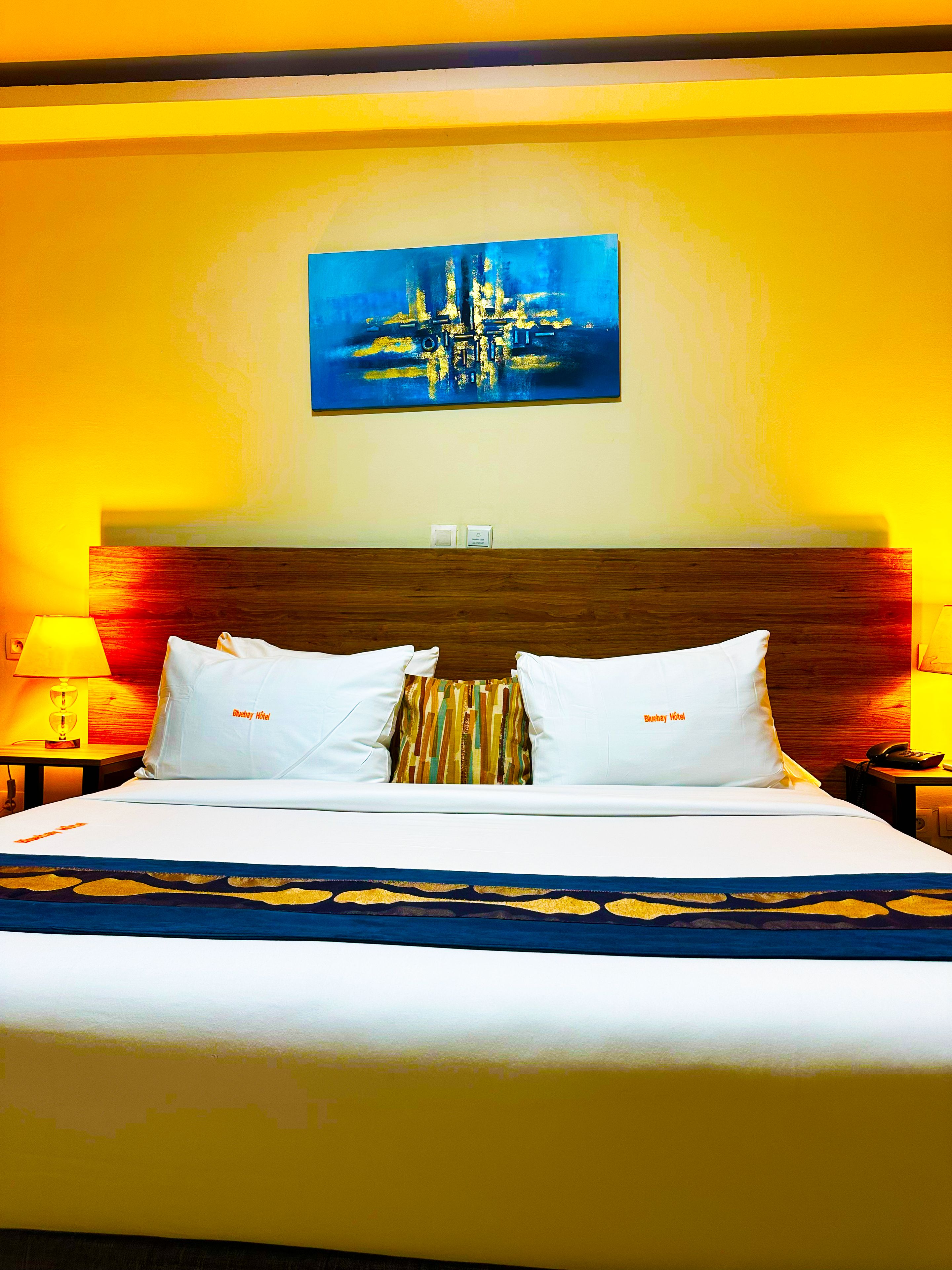 A hotel room with a large bed, two bedside lamps, a painting on the wall, and a wooden headboard.