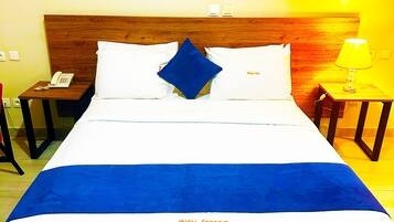 Une chambre d’hôtel avec un grand lit, une tête de lit en bois, une table de chevet avec une lampe, un téléphone et un tableau au mur.