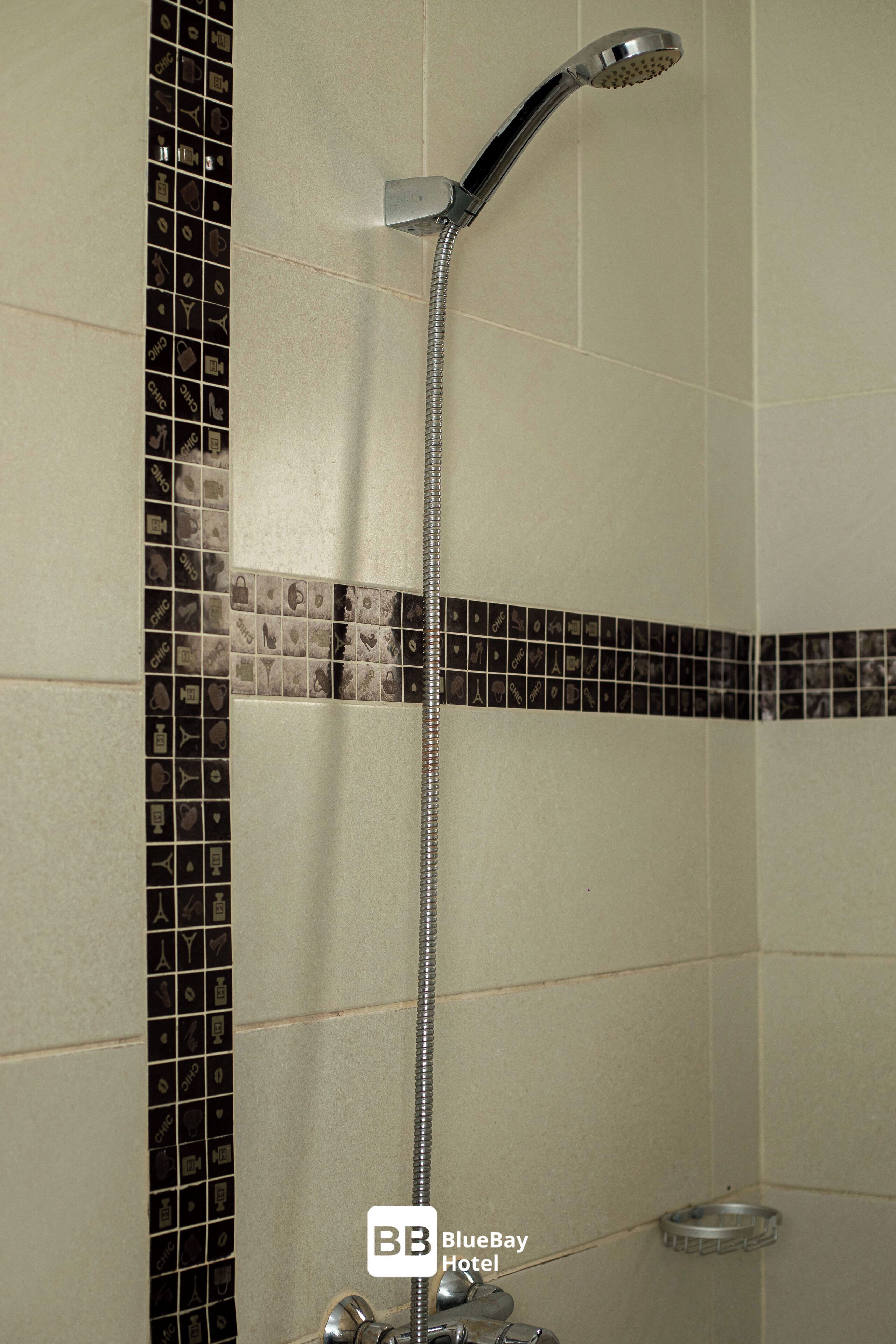 Ducha con cabezal cromado y manguera flexible, frente a un pared con borde de azulejos de diseño blanco y negro.