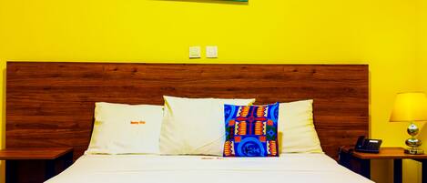 Una habitación de hotel con una cama grande, cabecera de madera, mesita de noche con lámpara y una obra de arte en la pared.