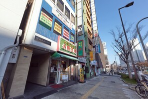Une vue de rue présentant différentes devantures de magasins, dont un restaurant avec un auvent vert et une enseigne.