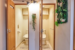 Une salle de bain avec deux toilettes, une douche, une porte en bois et une plante verte servant de décoration.