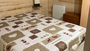 Un dormitorio con techo de madera, una cama con colcha estampada, un radiador blanco y una mesita de noche de madera.
