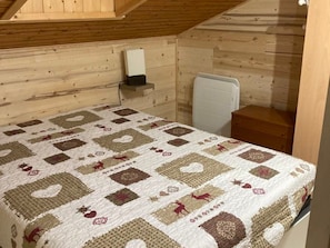 Ein Schlafzimmer mit Holzbalkendecke, einem Bett mit gemustertem Quilting, einem weißen Heizkörper und einem Nachttisch aus Holz.